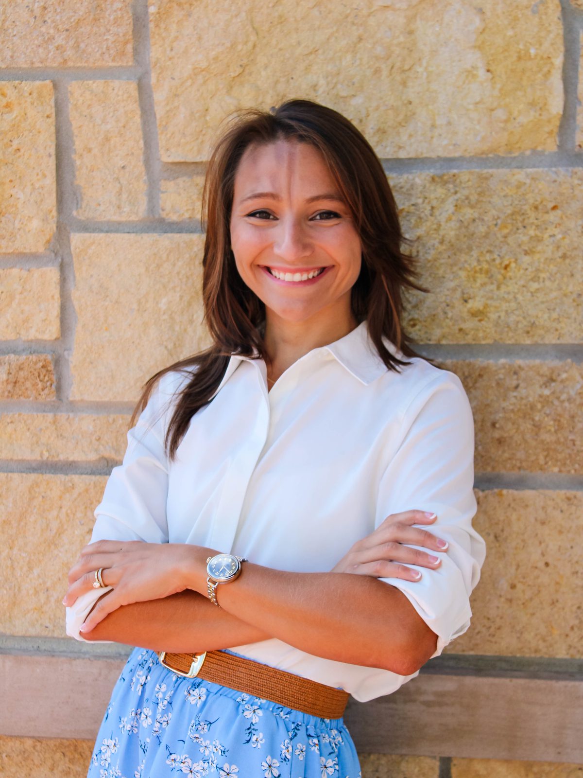 Dr. Abby Maidlow standing against a stone wall, arms folded, smiling.