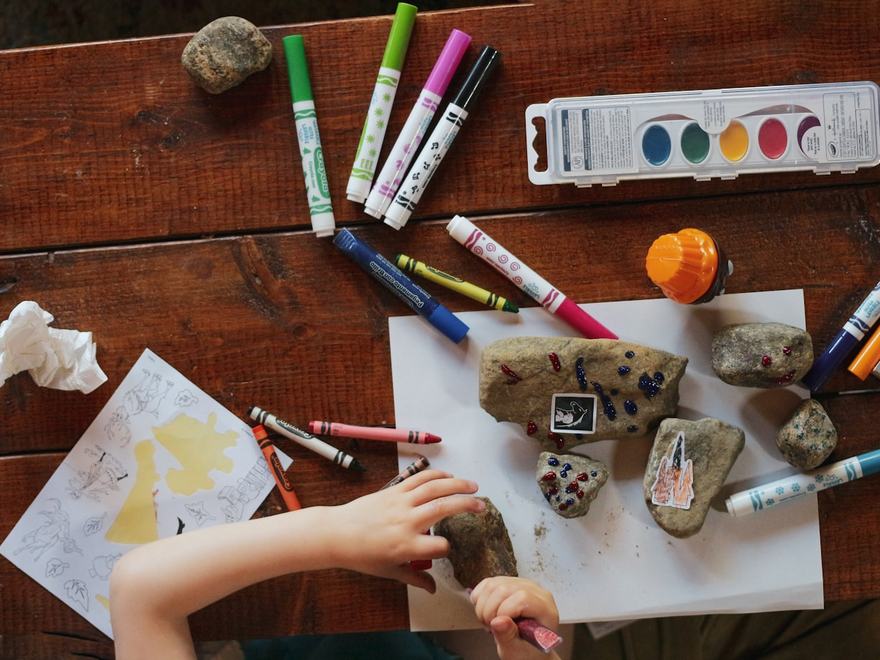 Crayons, paint and a child's drawing on a table.